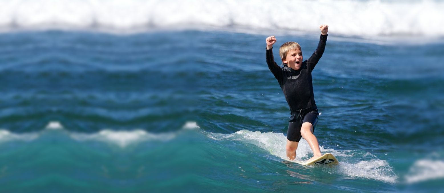 A young surfer rides whitewater with both fists in the air